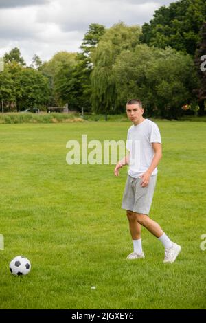 Ein neunzehnjähriger Jugendlicher, der in Einem öffentlichen Park Fußball spielt Stockfoto