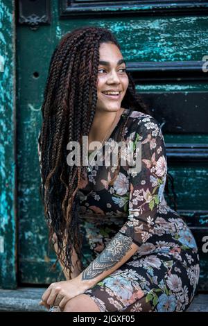 Porträt einer jungen kubanischen Frau, die lächelt und vor der Tür sitzt Stockfoto