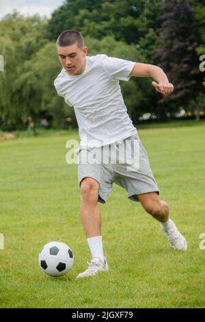 Ein neunzehnjähriger Jugendlicher, der in Einem öffentlichen Park Fußball spielt Stockfoto