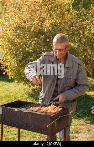 Älterer Mann, der an einem Herbsttag Fleisch gegrillt hat Stockfoto