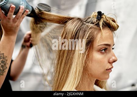 Barber bläst den Kunden Haare nach dem Haarschnitt im Friseurladen aus Stockfoto