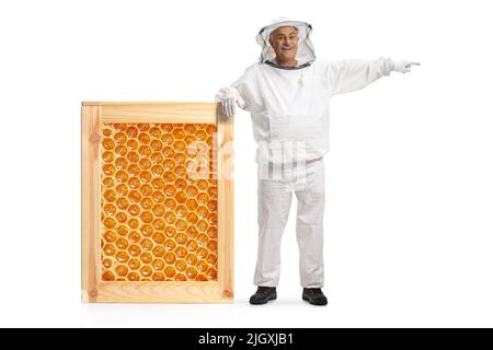 Reifer männlicher Bienenhalter in einer Uniform, der sich auf einen großen Wabenrahmen stützt und isoliert auf weißen Hintergrund zeigt Stockfoto