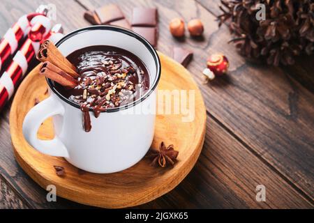 Heiße Schokolade. Hausgemachte würzige heiße Schokolade mit Zimt, zerkleinerte Haselnuss in emailliertem Becher auf altem Holzhintergrund. Gemütliche saisonale Feiertage. Stockfoto