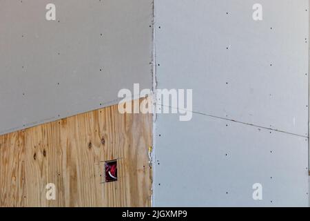 Bild einer Ecke in einem Neubau mit drei Trockenbauplatten und einer Trockenbauplatte aus Holz mit ausgeschnittener Steckdose. Stockfoto