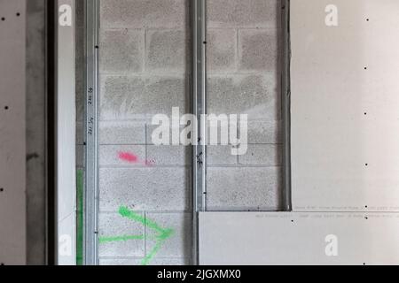 Trockenbauplatten, teilweise auf verzinkten Stahlrahmenstreben in einem Geschäftsgebäude installiert, das auf einer Wand aus Zunder-/Betonblöcken aufgestellt ist. Stockfoto