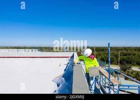Bauarbeiter, der Stuck auf die Instrumententafel/Dachkante/niedrige Attika eines Geschäftsgebäudes in der Nähe von Marco Island, Florida, anwendet Stockfoto