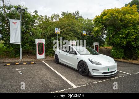 Tesla Supercharger Ladestation mit geparktem Tesla-Auto, Welcome Break Services Abington, Schottland, Großbritannien Stockfoto