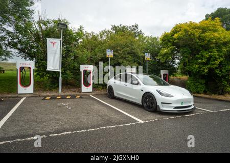 Tesla Supercharger Ladestation mit geparktem Tesla-Auto, Welcome Break Services Abington, Schottland, Großbritannien Stockfoto