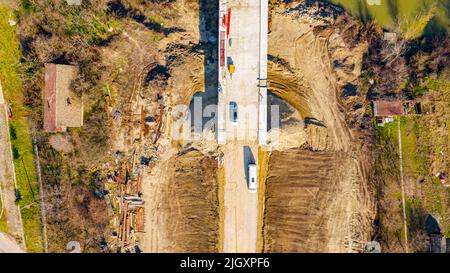 Oben Blick auf das Ende des neuen Grundstraßenfundaments, Bruch, Kies und Beginn der im Bau befindlichen Brücke, improvisiertes Alfresco-Lager Stockfoto