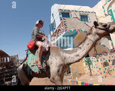 Touristen mittleren Alters reiten auf einem Kamel auf einem nubischen Dorf in Ägypten, Afrika Stockfoto