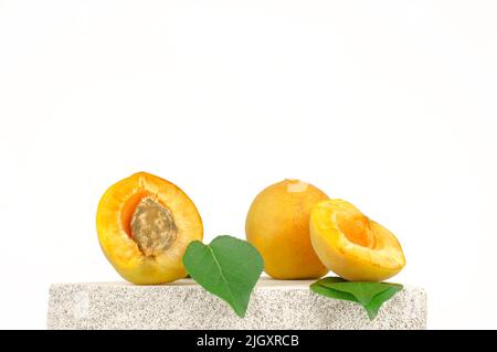 Frische Aprikosen und grüne Aprikosenblätter auf einem Podium aus Naturstein. Schaufenster für Werbeprodukte Stockfoto