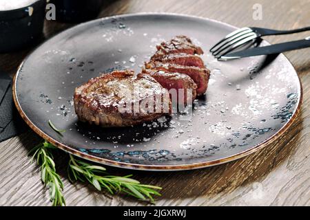 Nahaufnahme geschnittenes mittelseltenes Steak, serviert auf Teller mit Besteck. Hauptgericht, Restaurantgericht, Esskonzept Stockfoto