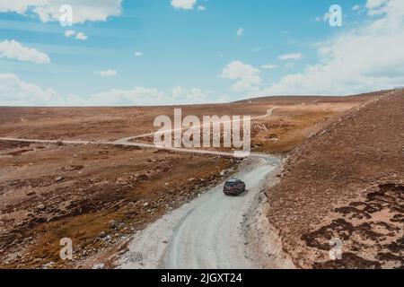 SUV fährt auf einer windigen, kurvigen, unbefestigten Straße durch das orangefarbene Hochplateau des Deosai-Nationalparks im Norden Pakistans Stockfoto