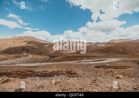 Autos fahren auf einer kurvigen Bergstraße durch trockenes Gelände im Deosai-Nationalpark in Pakistan Stockfoto