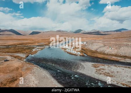 Weiße Zeltlager am Ufer des blauen Flusses im Deosai-Nationalpark in Pakistan an sonnigen Tagen, aus der Luft Stockfoto