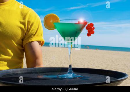 Kellnerhand hält Cocktail Blue Curacao mit Melonenlikör, Ananassaft, Johannisbeere und Orange auf dem Tablett Stockfoto