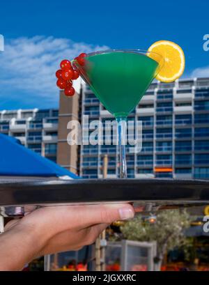 Kellnerhand hält Cocktail Blue Curacao mit Melonenlikör, Ananassaft, Johannisbeere und Orange auf dem Tablett Stockfoto