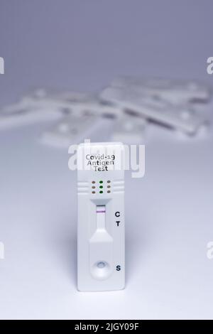 Ein Covid-19-Antigentest mit negativem Ergebnis, mit einem Stapel unfokussierter Tests im Hintergrund, auf weißem Hintergrund Stockfoto