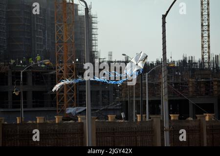 Giza, Ägypten, Juni 13 2022: Ein fliegender Drachen aus Kunststoff- und Weidenholz mit dem Hintergrund einer Baustelle mit Neubauten, Kränen und Äckern Stockfoto