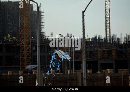 Giza, Ägypten, Juni 13 2022: Ein fliegender Drachen aus Kunststoff- und Weidenholz mit dem Hintergrund einer Baustelle mit Neubauten, Kränen und Äckern Stockfoto