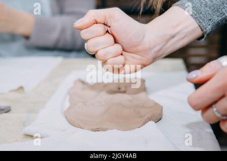 Weibliche Hände kneten Ton. Herstellung von keramischen Produkten in der Meisterklasse auf Keramik. Nahaufnahme. Stockfoto