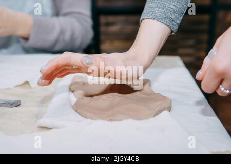 Weibliche Hände kneten Ton. Herstellung von keramischen Produkten in der Meisterklasse auf Keramik. Nahaufnahme. Stockfoto