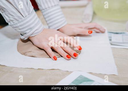 Weibliche Hände kneten Ton. Herstellung von keramischen Produkten in der Meisterklasse auf Keramik. Nahaufnahme. Stockfoto