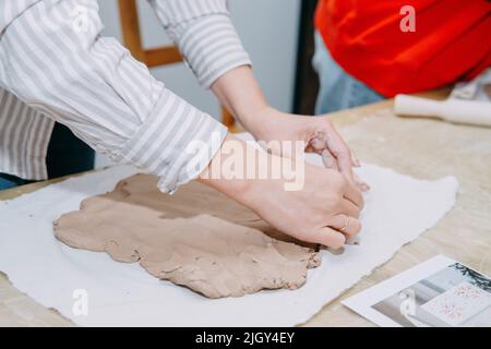 Weibliche Hände kneten Ton. Herstellung von keramischen Produkten in der Meisterklasse auf Keramik. Nahaufnahme. Stockfoto