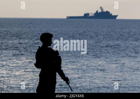 Schweden. 7.. Juni 2022. Eine US-Marine, die dem Amphibiendock-Landungsschiff USS Gunston Hall (LSD 44) zugeordnet ist (im Hintergrund zu sehen), steht an einem Strand auf der schwedischen Insel Gotland während der Übung BALTOPS 22. Die von den US-Marinestreitkräften Europa-Afrika geleitete und von den Naval-Streikkräften und der NATO durchgeführte Übung bietet eine einzigartige Ausbildungsmöglichkeit, um kombinierte Reaktionsfähigkeiten zu stärken, die für die Wahrung der Schiffs- und Sicherheitsfreiheit in der Ostsee von entscheidender Bedeutung sind. (Bild: © Rob Kunzig/USA Marines/ZUMA Press Wire Service) Stockfoto