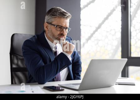 Fokussierter Geschäftsmann Mittleren Alters, Der Während Der Arbeit Im Büro Auf Den Laptop-Bildschirm Schaut Stockfoto