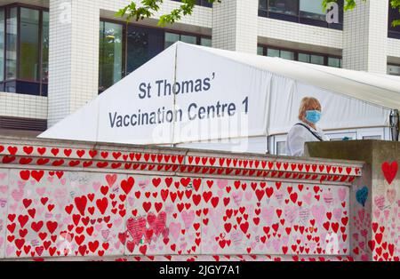 London, England, Großbritannien. 13.. Juli 2022. Eine Frau, die eine schützende Gesichtsmaske trägt, steht über der National Covid Memorial Wall vor dem Impfzentrum des St. Thomas' Hospital, da die britischen Covid-Todesfälle über 200.000 liegen. Tausende rote Herzen wurden an die Wand gegenüber dem Parlament gemalt, eines für jedes Leben, das durch das Coronavirus verloren wurde. (Bild: © Vuk Valcic/ZUMA Press Wire) Stockfoto