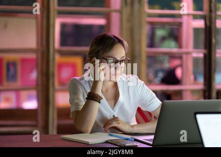 Verärgert Studentin in Brille sitzt am Schreibtisch mit Laptop in Coworking, müde vom Lernen Stockfoto