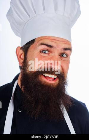 Bärtiger Mann in Uniform. Männlicher Koch oder Bäcker in weißem Hut und Schürze. Porträt eines lächelnden Küchenchefs. Kochen. Stockfoto