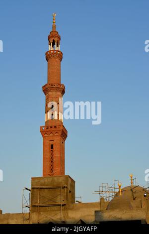 Ein hohes Minarett mit goldenem Ornament einer Moschee, die im Bau ist, Minarett oder Turm, der nach Himmel, islamischer Religion und Architektur strebt Stockfoto