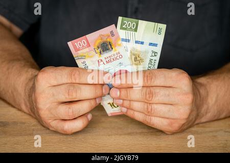 Mexiko Geld, ein Mann in einem Hemd hinter einem Schreibtisch hält 100 und 200 Pesos Banknoten in der Hand, Business Investments, Creative Financial Concept Stockfoto