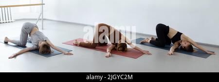 Gruppe junger sportlicher Menschen, die Yoga-Unterricht mit Lehrer, Stretching in Child Exercise, Balasana Pose, Workout, Nahaufnahme in der Halle üben Stockfoto