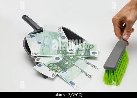 Hundert Euro-Banknoten werden mit einem Pinsel in eine Müllkippschale geschwemmt. Euro-Krise, Rückgang des Wertes der Währungsabwertung Stockfoto