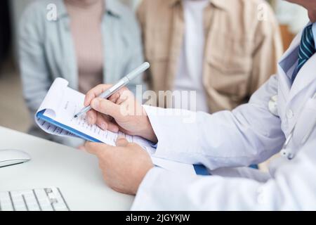 Nahaufnahme eines nicht erkennbaren Arztes, der am Tisch sitzt und das Patientenformular für die Registrierung im Krankenhaus ausfüllt Stockfoto