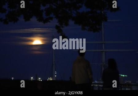 Hamburg, Deutschland. 13.. Juli 2022. Der Vollmond steigt am Abend über dem Hamburger Hafen auf. Gleichzeitig ist der Mond nahe an der Erde, weshalb er als Supermond bezeichnet wird. Kredit: Marcus Brandt/dpa/Alamy Live Nachrichten Stockfoto