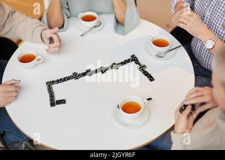 Eine Gruppe von nicht erkennbaren älteren Freunden, die am Tisch sitzen und bei einer Tasse Tee im Pflegeheim Dominosteine spielen Stockfoto