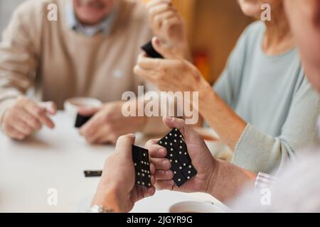 Nahaufnahme eines nicht erkennbaren älteren Mannes, der Dominosteine anschaut und an Strategie denkt, während er mit Freunden Dominosteine spielt Stockfoto