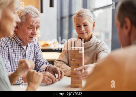 Die Gruppe der Inhalte konzentrierte ältere Menschen, die im Pflegeheim am Tisch saßen und zusammen Jenga spielten Stockfoto