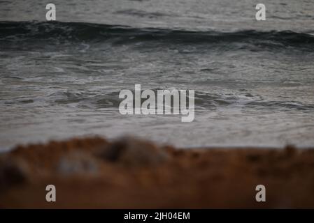 Ein selektiver Fokus auf Meereswellen von verschwommenem Sandstrand Stockfoto