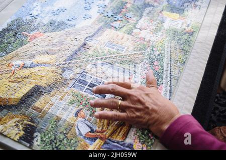 NAHAUFNAHME DER HAND EINER ÄLTEREN DAME IN EINEM ALTERSHEIM, DIE EIN PUZZLE MACHT Stockfoto