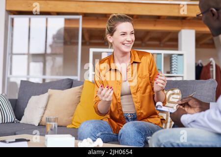 Fröhlich aufgeregt junge Frau in lässigem Outfit sitzen auf Couch und gestikulieren Hände, während lachen und sprechen mit Therapeuten bei der Sitzung Stockfoto