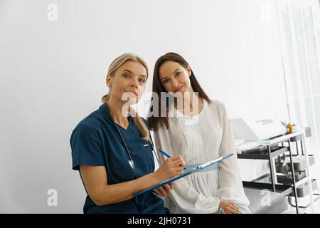 Der Arzt füllt die Form des medizinischen Berichts der Patienten während des Termins und der Suche nach der Kamera aus Stockfoto