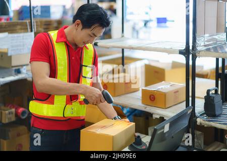 Asiatischer Lagerarbeiter mit Computer und Barcodescanner im Lager scannen an der Box liefern an den Kunden. Stockfoto
