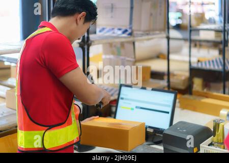 Asiatischer Lagerarbeiter mit Computer und Barcodescanner im Lager scannen an der Box liefern an den Kunden. Stockfoto