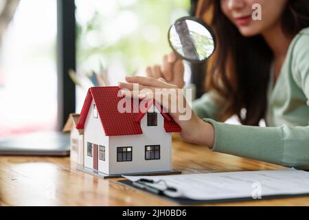 Eine Frau, die Lupe hält und das Hausmodell überprüft.Immobilienhaus Bewertung und Inspektionskonzept. Stockfoto