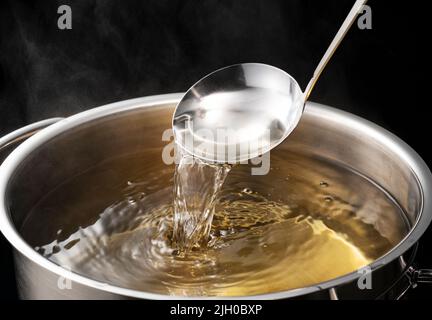 Dashi, Suppenbrühe und die Grundlagen der japanischen Küche. Schwarzer Hintergrund. Dampf. Aushöhlung mit einer Schöpfkelle. Stockfoto